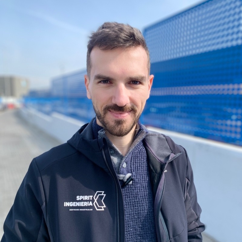 Retrato de ingeniero con chaqueta de Spirit Ingeniería, fondo industrial azul